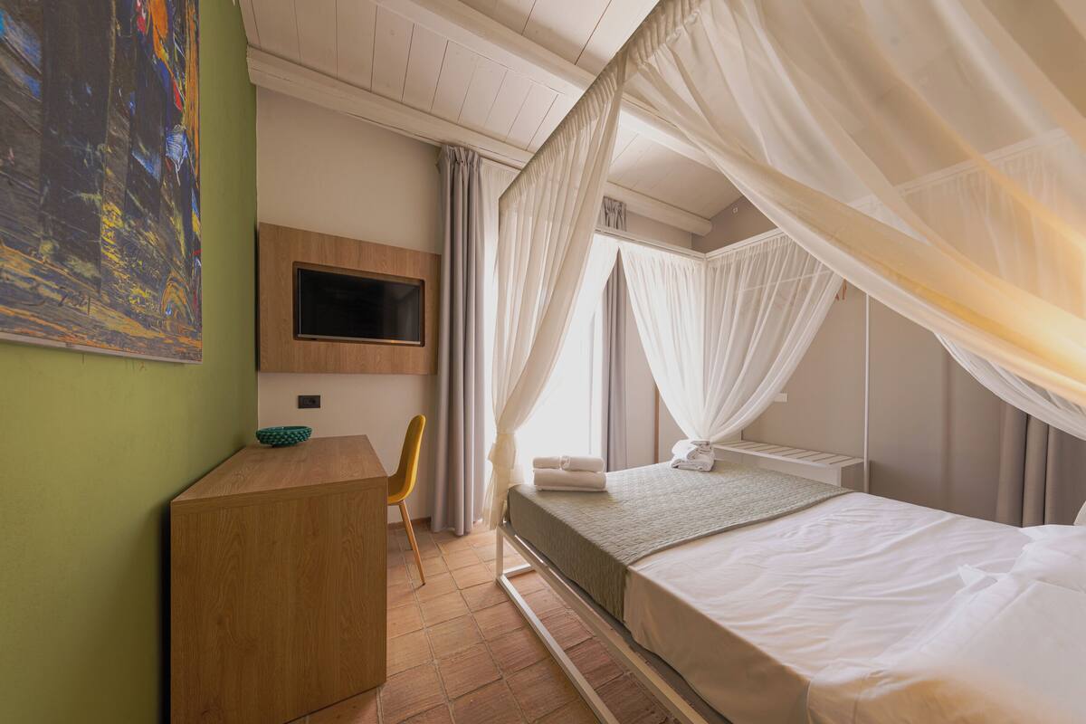 A bedroom with a bed, a desk, a chair, a television, and a painting on the wall.