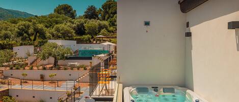 A hot tub adjacent to a white building with a balcony, surrounded by a landscaped garden and a pool area.