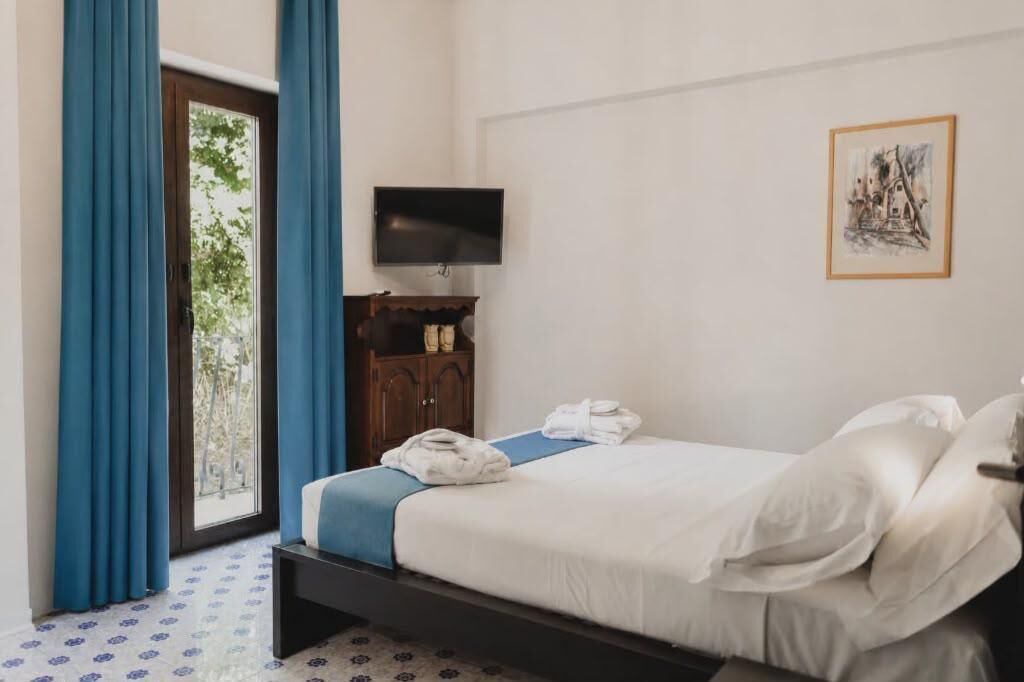 A hotel room with a bed, a TV, a wardrobe, and a window with curtains.