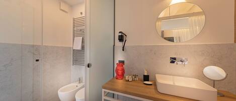 A modern bathroom with a glass shower enclosure, a bidet, a wooden vanity with a sink, and a round mirror.