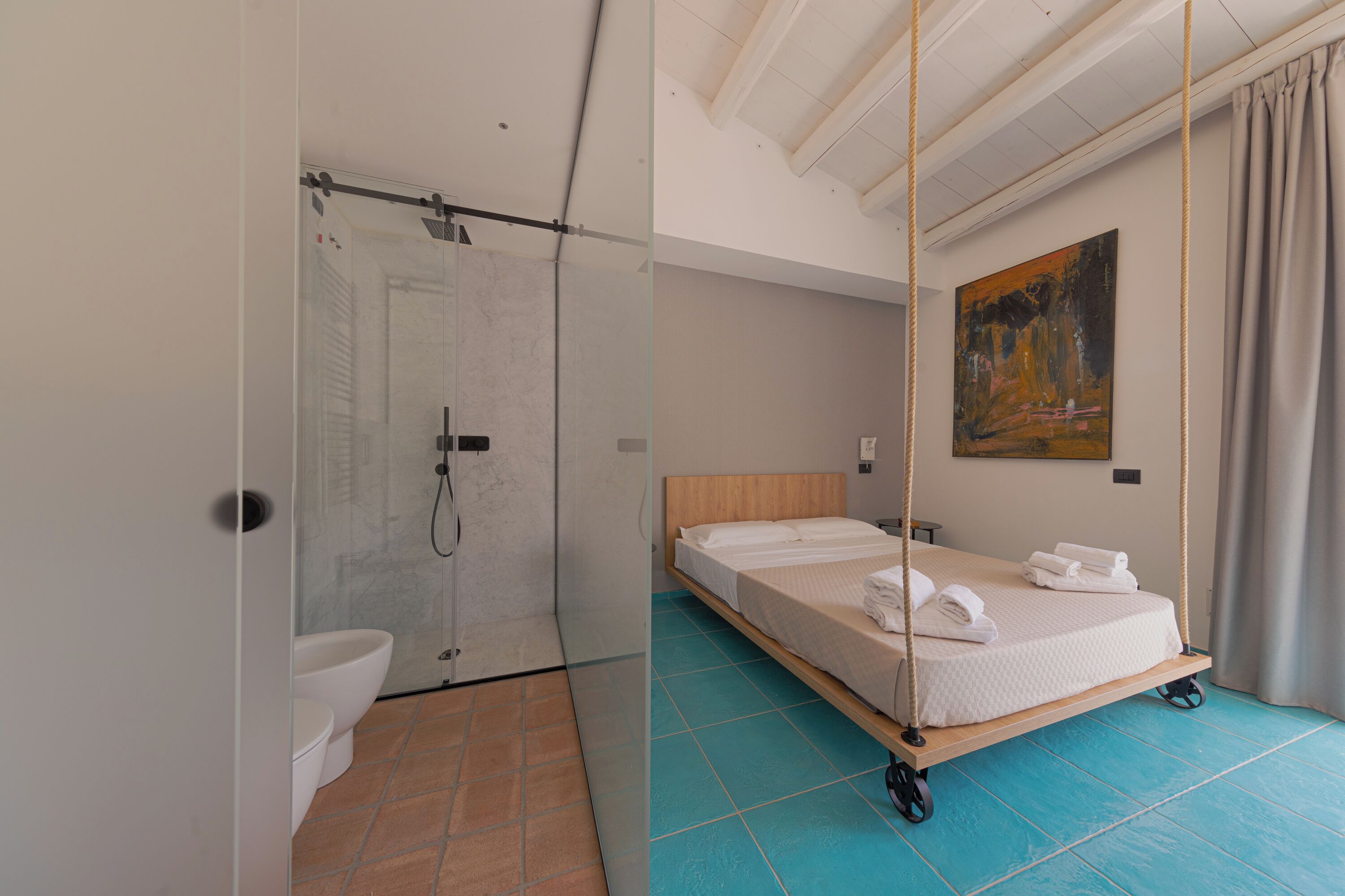 A modern hotel room with a glass-enclosed shower, a wooden bed with a mattress and pillows, and a painting on the wall.
