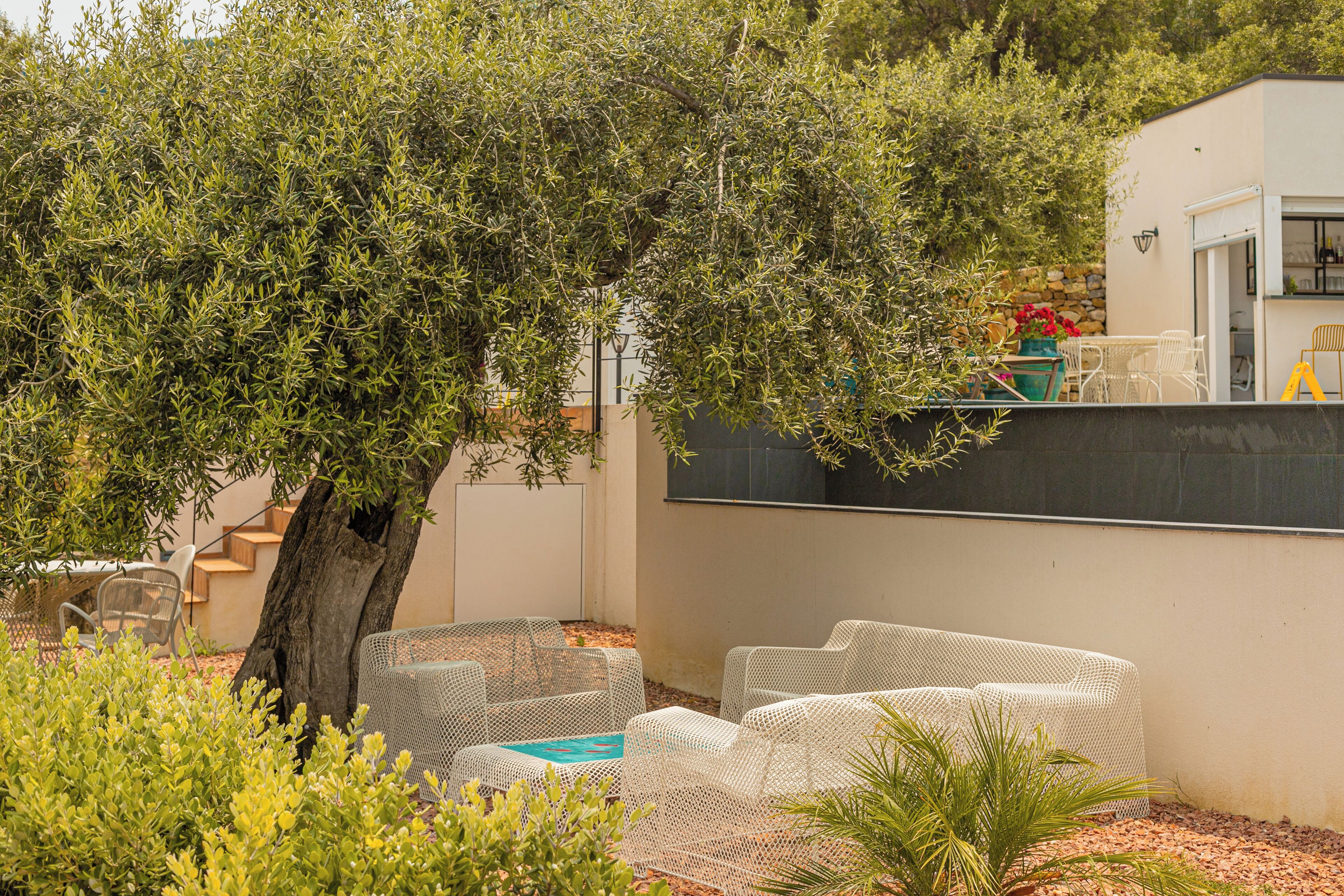 An outdoor seating area with white wicker furniture, a tree, and a building with a stone wall and a door.