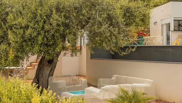 An outdoor seating area with white wicker furniture, a tree, and a building with a stone wall and a door.