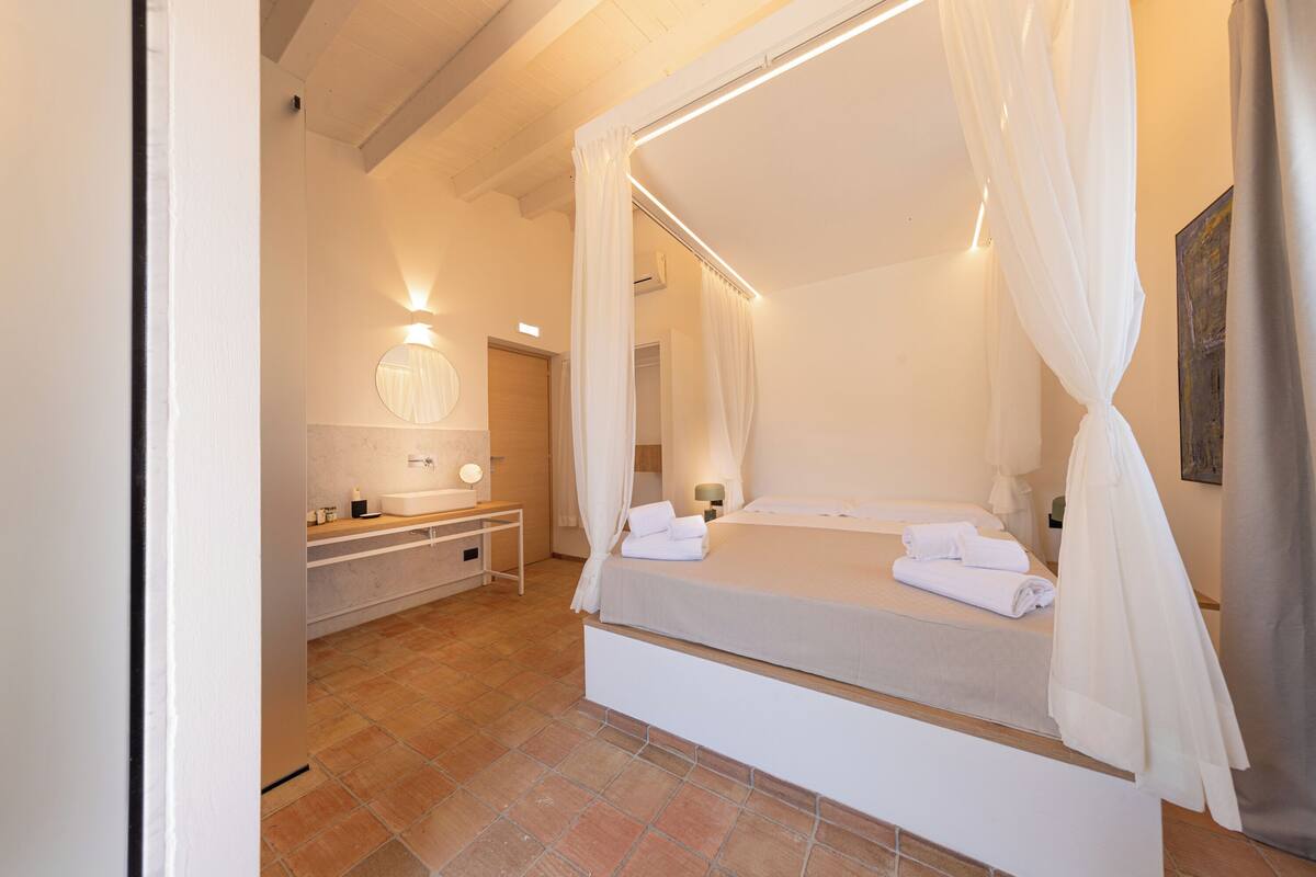 A bedroom with a four-poster bed, a vanity with a mirror, and a bedside table.