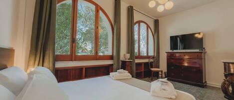 A hotel room with a large bed, a TV, a dresser, and a window with a view of trees.