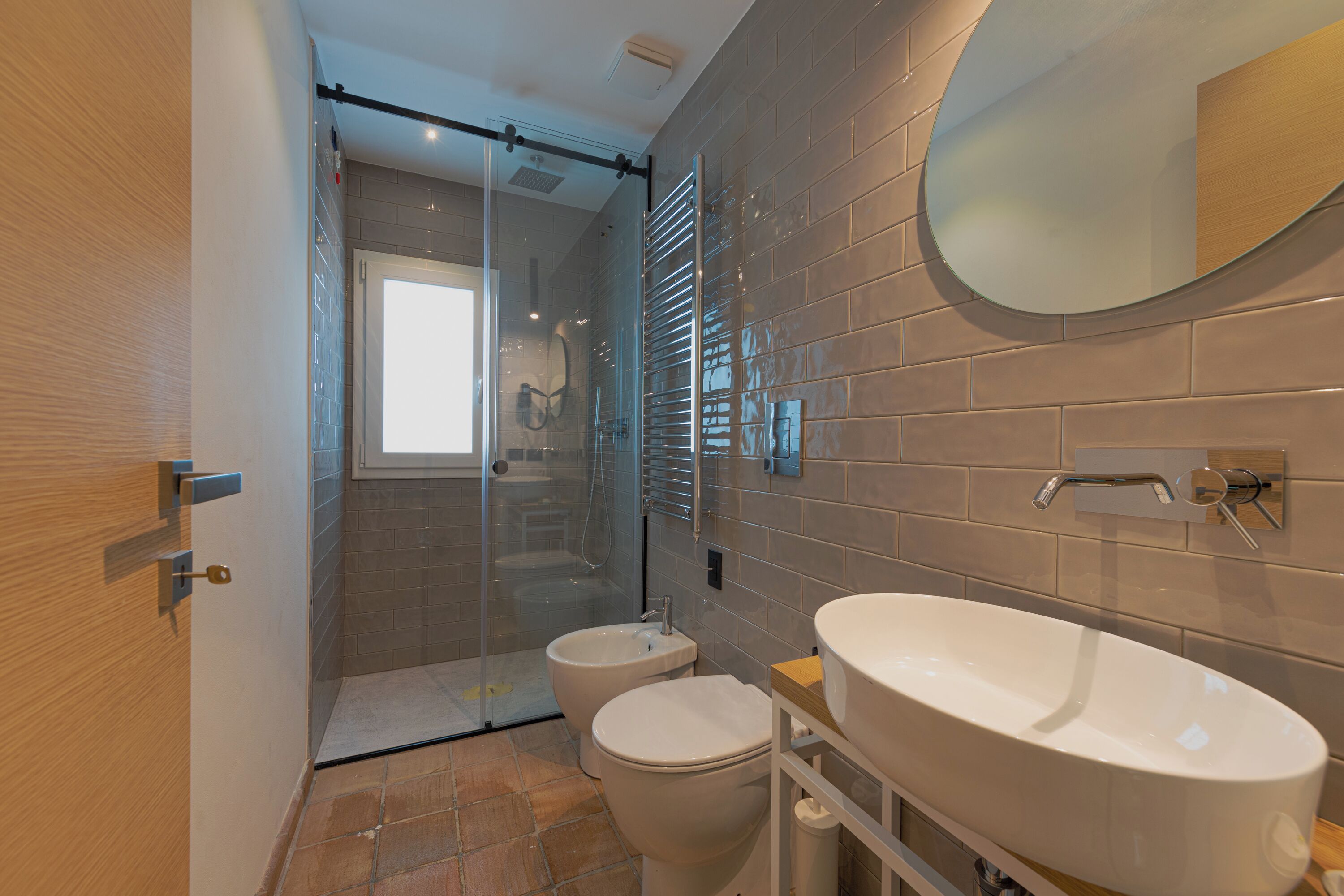 Une salle de bain moderne dotée d’une douche à parois de verre, d’un grand miroir ovale et d’un meuble-lavabo à deux vasques.