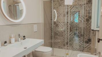 Un baño moderno con ducha, inodoro, bidé y un espejo grande.