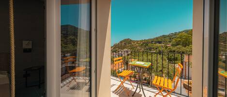 A balcony with a table and chairs, a view of a hilly landscape, and a railing.
