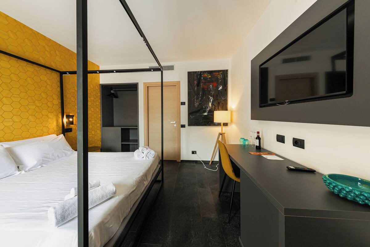 A modern hotel room with a bed, a desk, a mirror, and a TV.