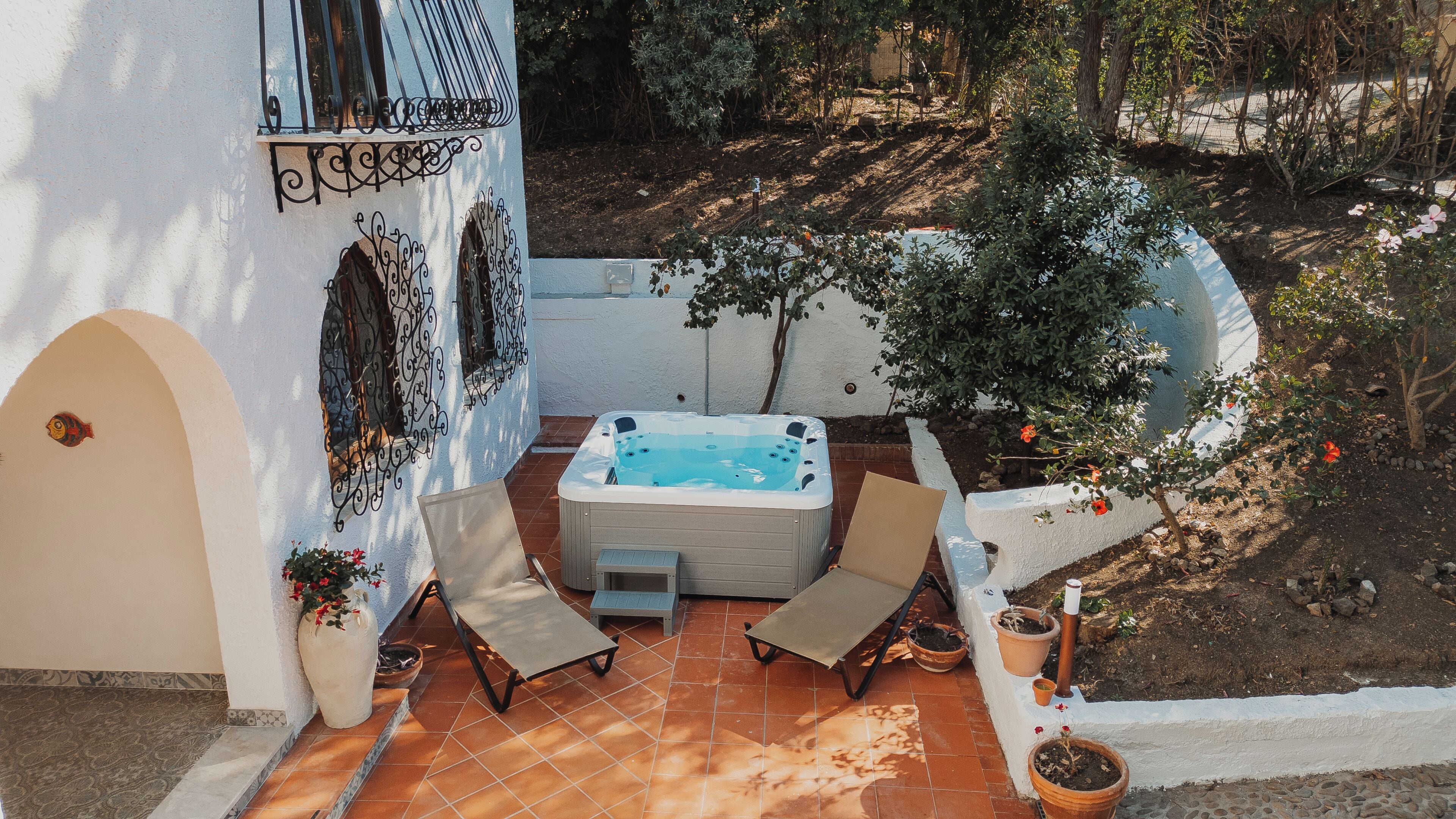 Un jacuzzi con dos sillones reclinables, una mesita y plantas en macetas en un jardín.