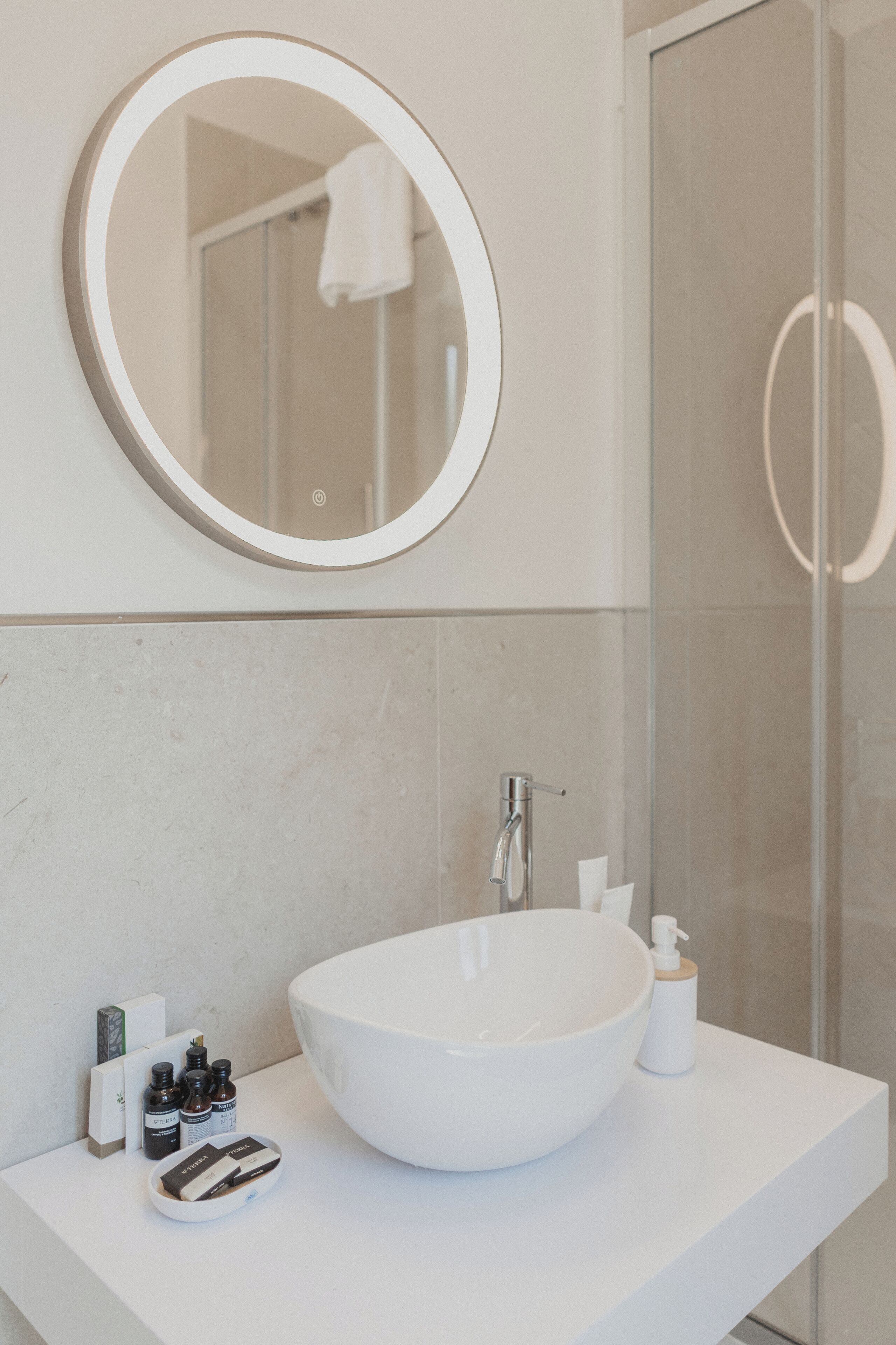 Un baño con lavabo blanco, espejo redondo y cabina de ducha de vidrio.