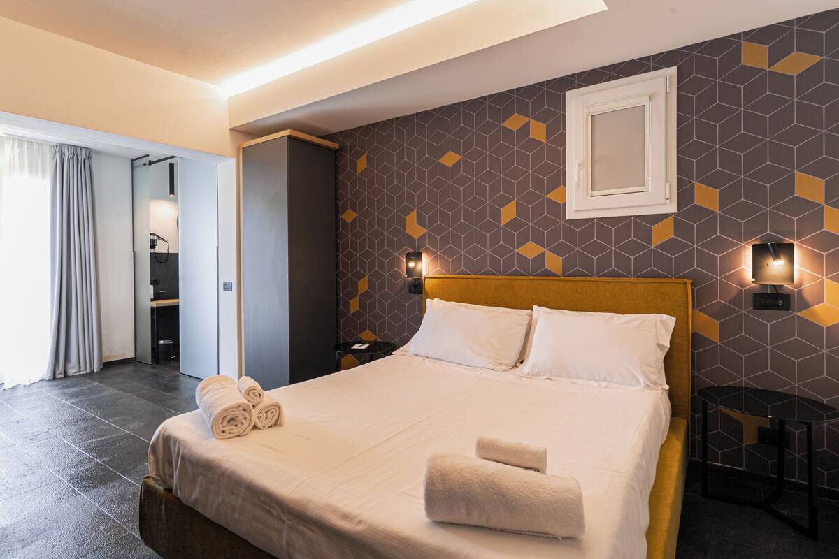 A hotel room with a large bed, a headboard, a nightstand, and a wall-mounted light fixture.