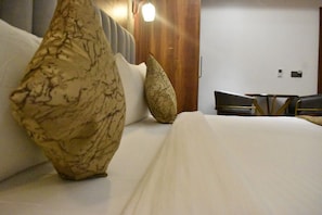 A hotel room with a bed, two large decorative pillows, a wooden headboard, a small table, and a chair. - 3AG HOTEL & RESORT (Faizabad)