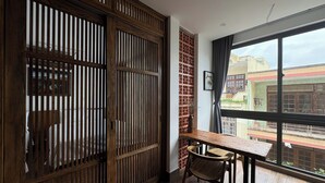 Una habitación con un separador de madera, una mesa de comedor con sillas y un ventanal con vistas a edificios.