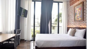 Habitación de hotel con cama, escritorio, silla, televisor en la pared y balcón con cortinas.