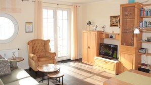 A living room with a sofa, armchair, and coffee table. There is a television and a cabinet with glassware. - 4-star apartment near the beach with two balconies (Ostseebad Boltenhagen)
