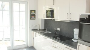 A modern kitchen with white cabinets, a black countertop, a built-in microwave, and a coffee maker. - 4-star apartment near the beach with two balconies (Ostseebad Boltenhagen)