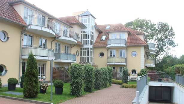 A multi-story residential building with balconies, a central tower, and a brick pathway leading to a garage. - 4-star apartment near the beach with two balconies (Ostseebad Boltenhagen)