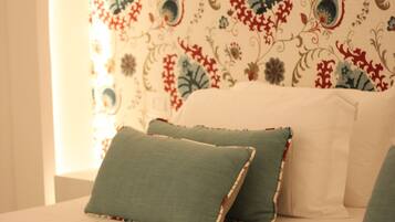 Una cama con papel tapiz estampado con motivos florales, dos almohadas verdes y un cabecero blanco.