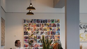 Habitación con una pared llena de viñetas de cómics, una persona sentada y una planta al frente.