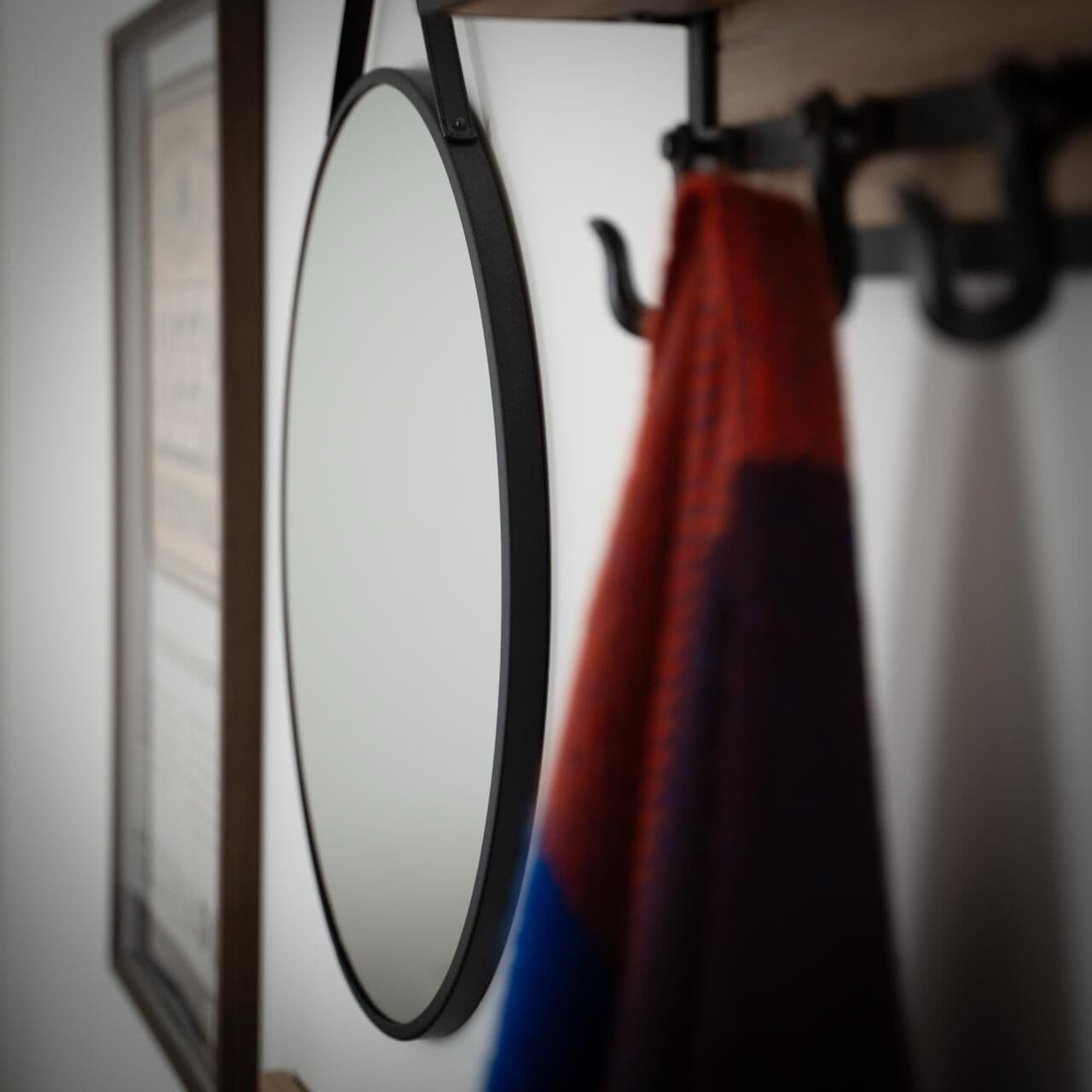 A framed picture on the wall, a mirror, and a red and blue object hanging on a hook.