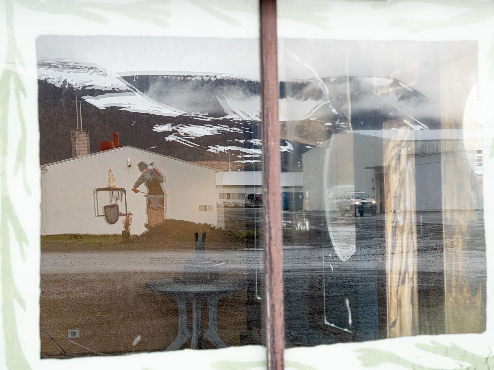 Une vue par la fenêtre sur un bâtiment, avec une montagne enneigée en arrière-plan.