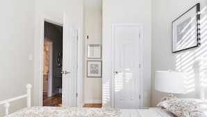 A bedroom with a bed, a bedside table, a lamp, and a door leading to another room.