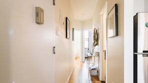 A hallway with a ceiling-mounted air purifier, framed pictures on the walls, a table with a basket, and a refrigerator.