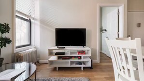 A modern living room with a flat-screen TV on a white TV stand, a potted plant, and a glass table.