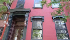 A red building with a brown door and two windows with metal bars.