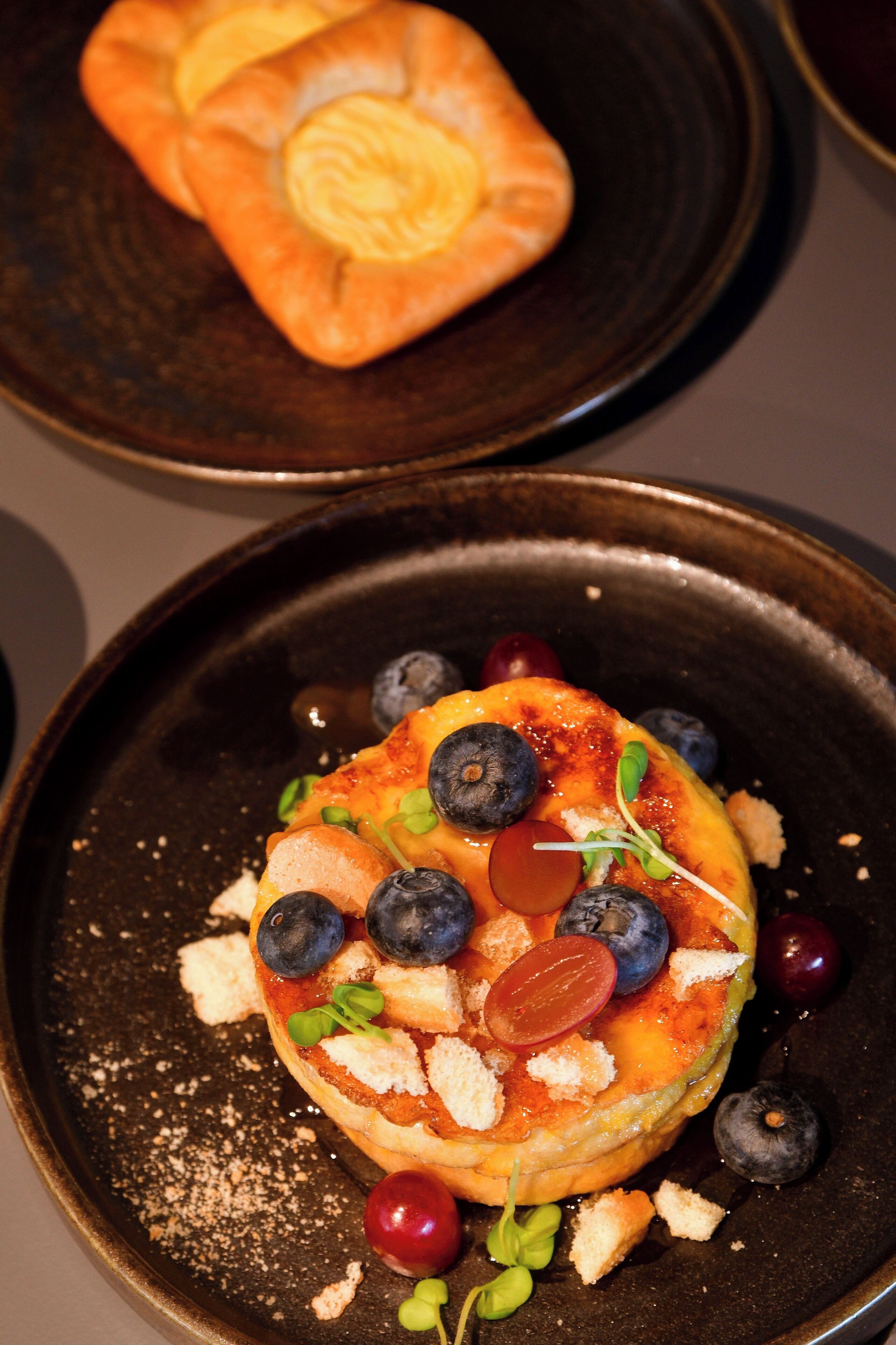 A dessert with blueberries, grapes, and a pastry on a dark plate.