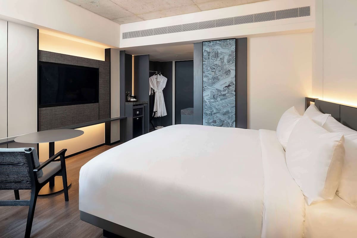 Une chambre d’hôtel moderne avec un grand lit, un téléviseur à écran plat, une petite table avec une chaise et un peignoir accroché à un crochet.