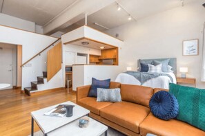 A modern interior with a sofa, a coffee table, a bed with pillows, a staircase, and a kitchen area. - Stylish Studio in Centre by Zodiak Stay (Auckland)