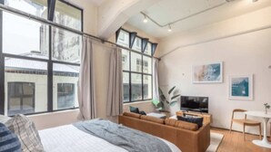 Moderni hotellihuone, jossa on suuri sänky, sohva, televisio ja ruokailutila.