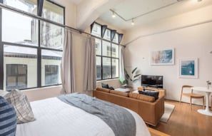 A modern hotel room with a large bed, a sofa, a TV, and a dining area. - Central stylish studio in CBD by Zodiak Stays (Auckland)