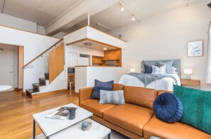 A modern living room with a sofa, a coffee table, and a bed with a headboard. There is a staircase leading to an upper level. - Central stylish studio in CBD by Zodiak Stays (Auckland)