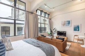 A modern hotel room with a large bed, a sofa, a TV, and a dining area. - Stylish Studio in Centre by Zodiak Stay (Auckland)