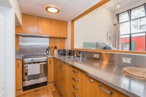A compact kitchen with wooden cabinets, stainless steel appliances, and a large window providing a view of the outside. - Stylish Studio in Centre by Zodiak Stay (Auckland)