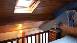 A room with a sloped ceiling, a skylight, a wooden staircase, a bed, a nightstand, and a wall-mounted lamp.