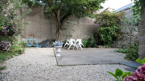 A courtyard with a gravel path, white chairs, and a concrete area.