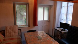 A room with a bed, a table with a plastic cover, a TV on a stand, and a window with curtains.