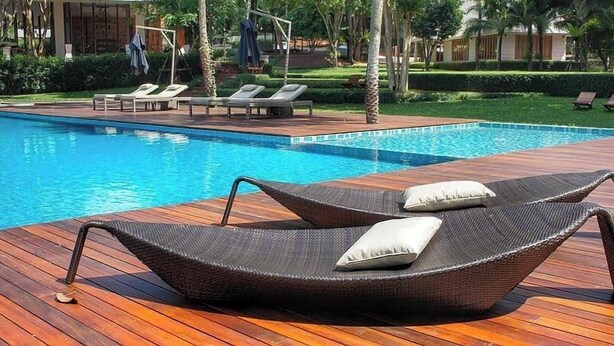 A poolside area with a wooden deck, lounge chairs, and a swimming pool. - Mic - Della Apartment  (Enugu)