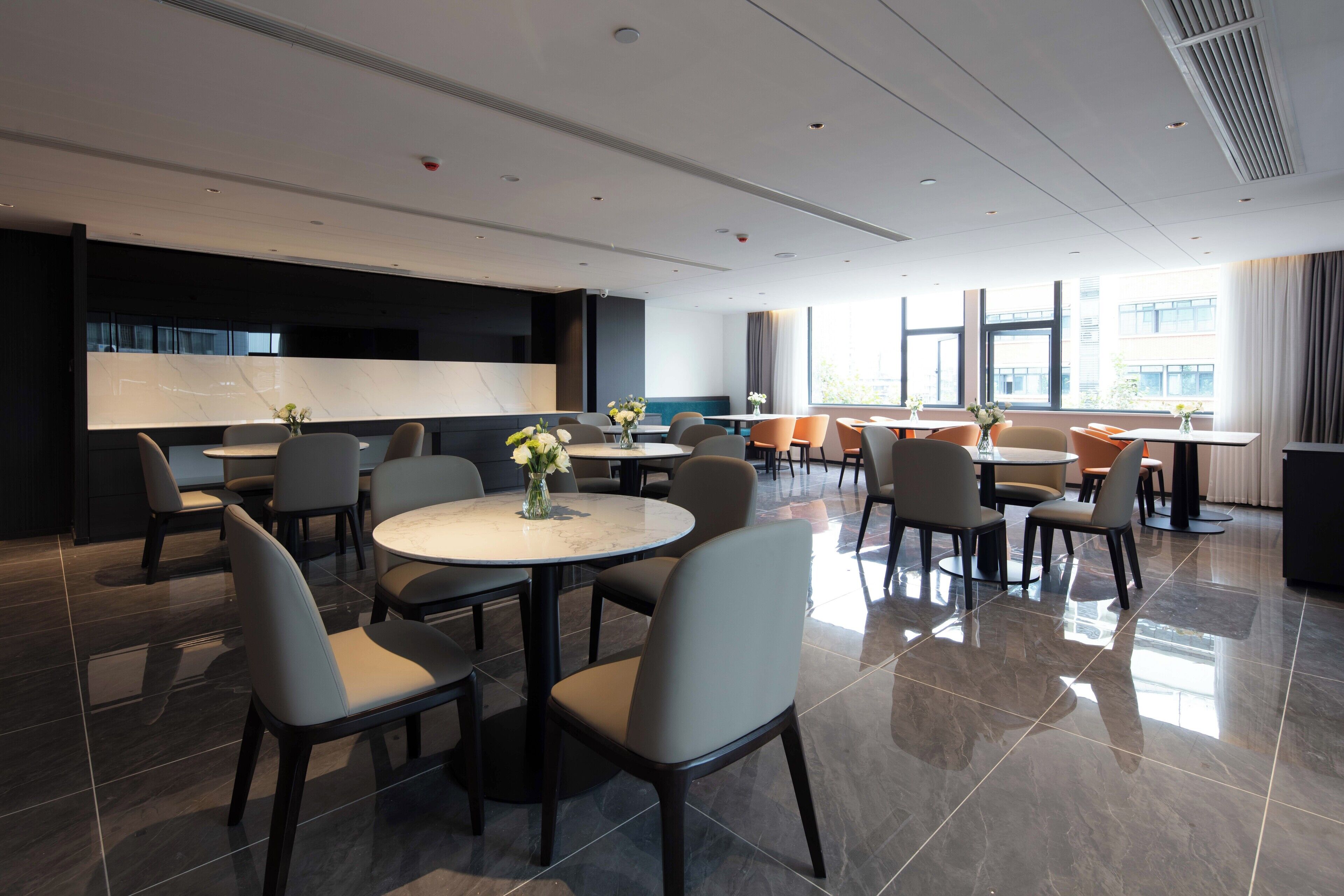 A modern hotel dining area with round tables and chairs, large windows, and a clean, minimalist design.