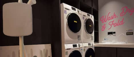 Een wasserette met een grote wasmachine en droger die aan de muur bevestigd zijn, een kledingrek en een decoratieve wand met cactussen.