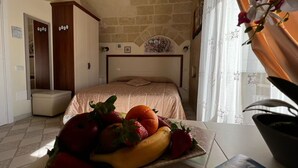 A bedroom with a bed, a wardrobe, a small table with fruit, and a window with curtains. - In the heart of the Sassi of Matera at 500 mt. from the historic center, apartment Deluxe (Matera)