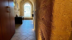 A hallway with stone walls and a tiled floor leading to a door with a window. - In the heart of the Sassi of Matera at 500 mt. from the historic center, apartment Deluxe (Matera)