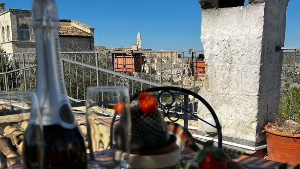 A table with a bottle of wine, glasses, and a basket of fruit on a rooftop terrace with a view of buildings and a stone structure. - In the heart of the Sassi of Matera at 500 mt. from the historic center, apartment Deluxe (Matera)