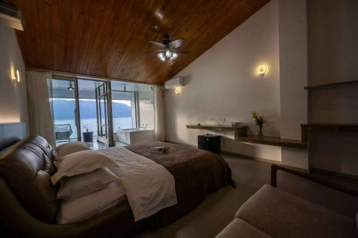 A bedroom with a large bed, a ceiling fan, a bedside table, and a view through a glass door.