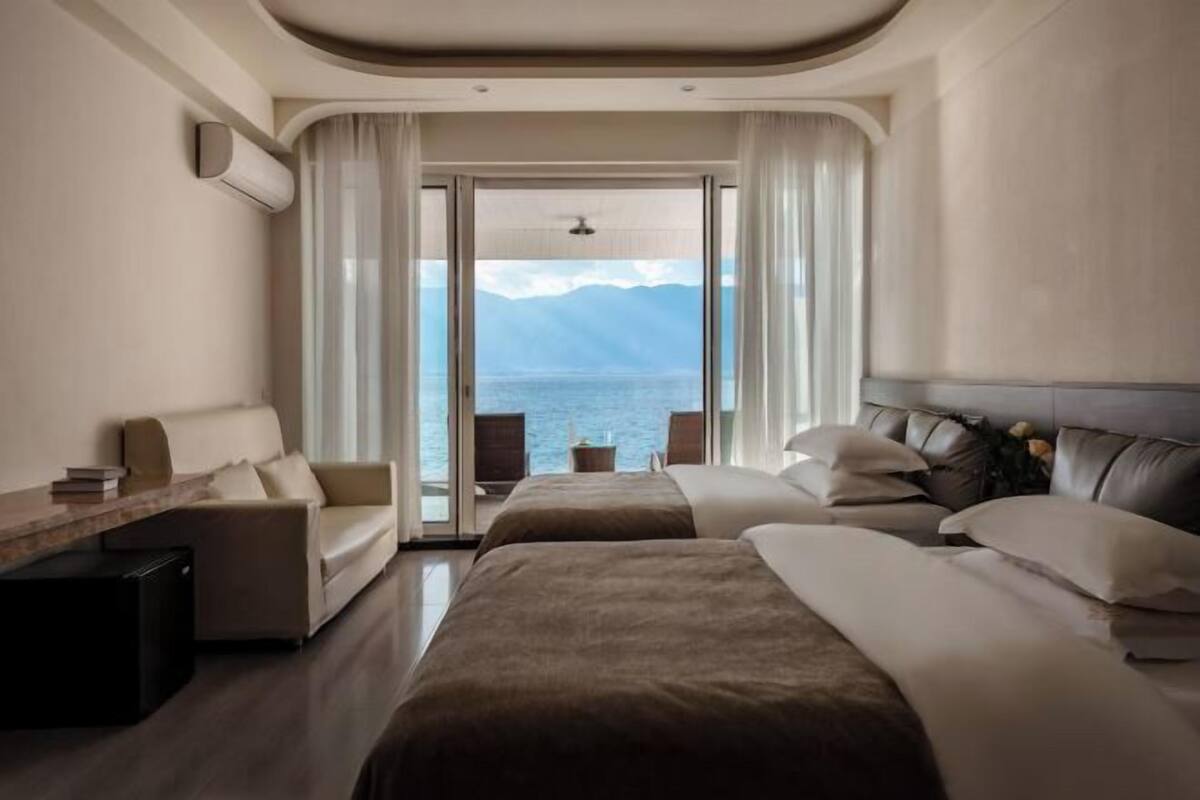 A hotel room with a bed, a sofa, a desk, and a view of the sea.