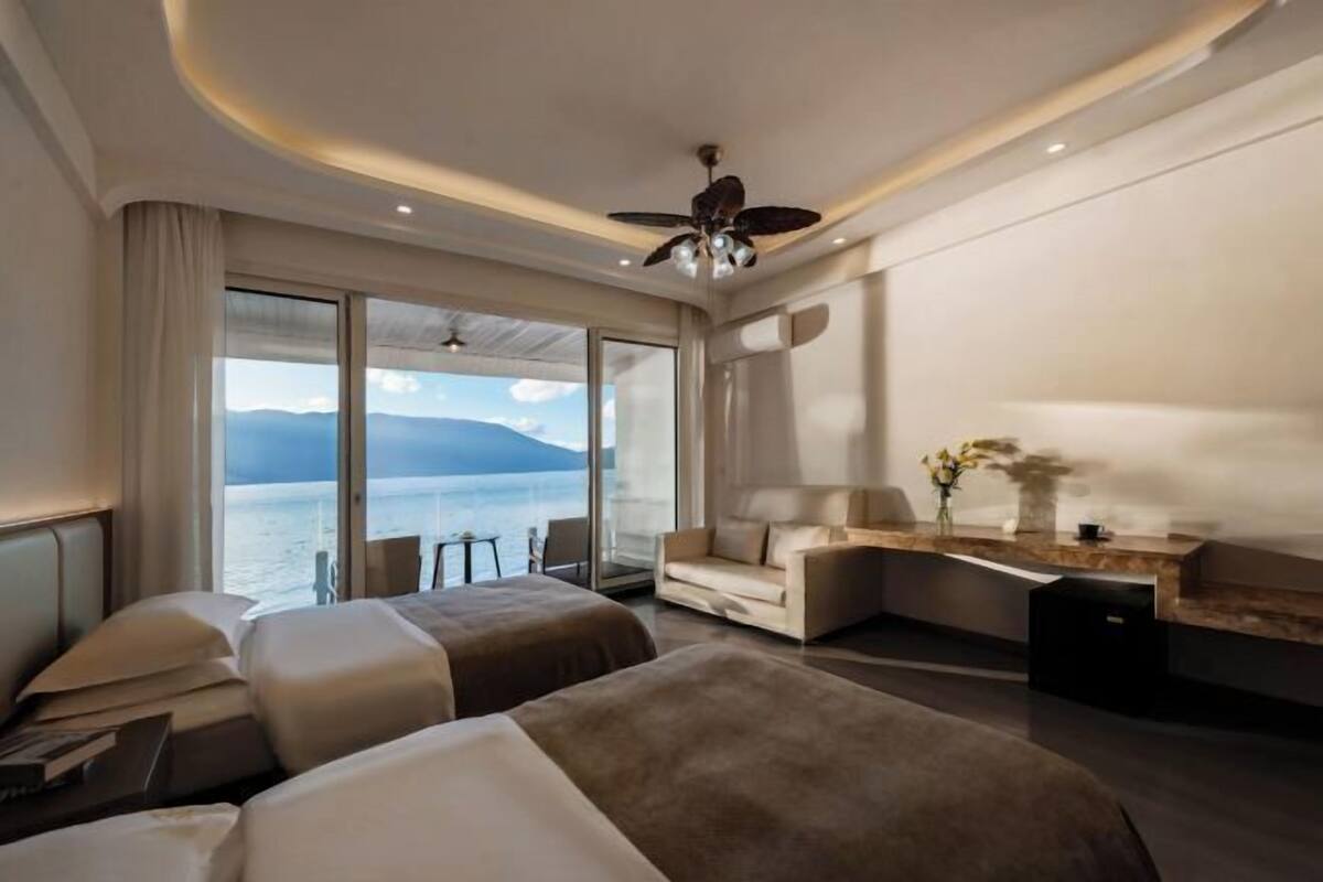 A modern hotel room with a large bed, a sofa, a desk, and a view of the sea.